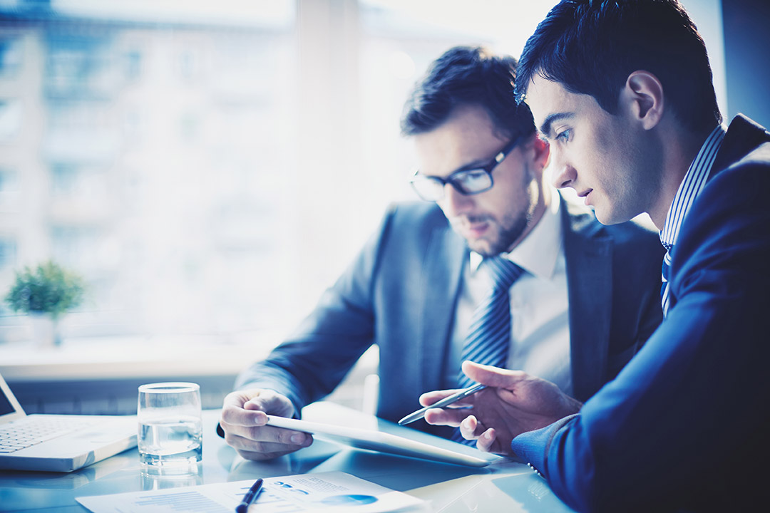 Two business professionals discussing HRSA 340B program strategies while reviewing documents and a tablet in a modern office setting.