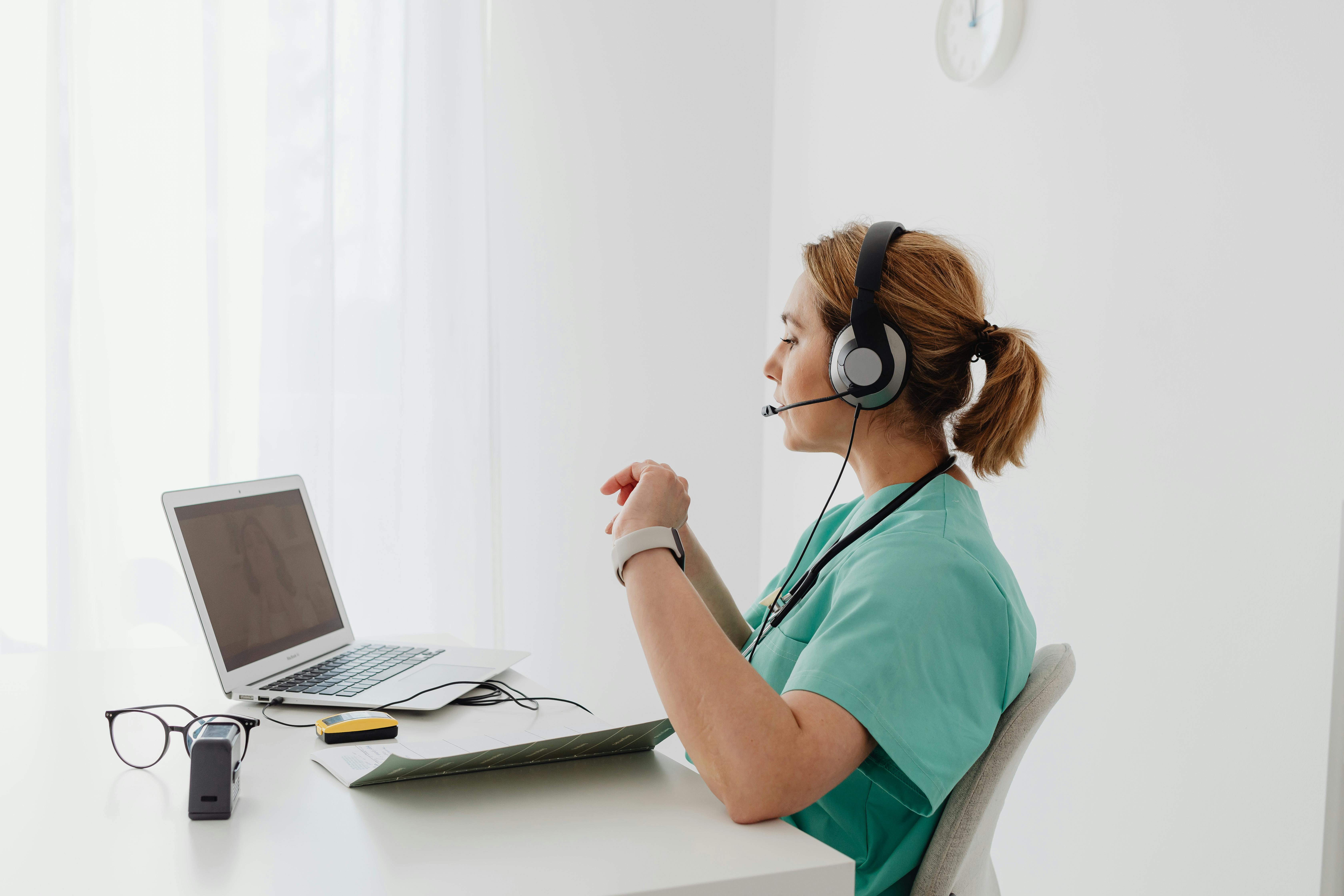 Healthcare professional in scrubs using a headset and laptop for telehealth consultations, emphasizing remote patient support in 2025.