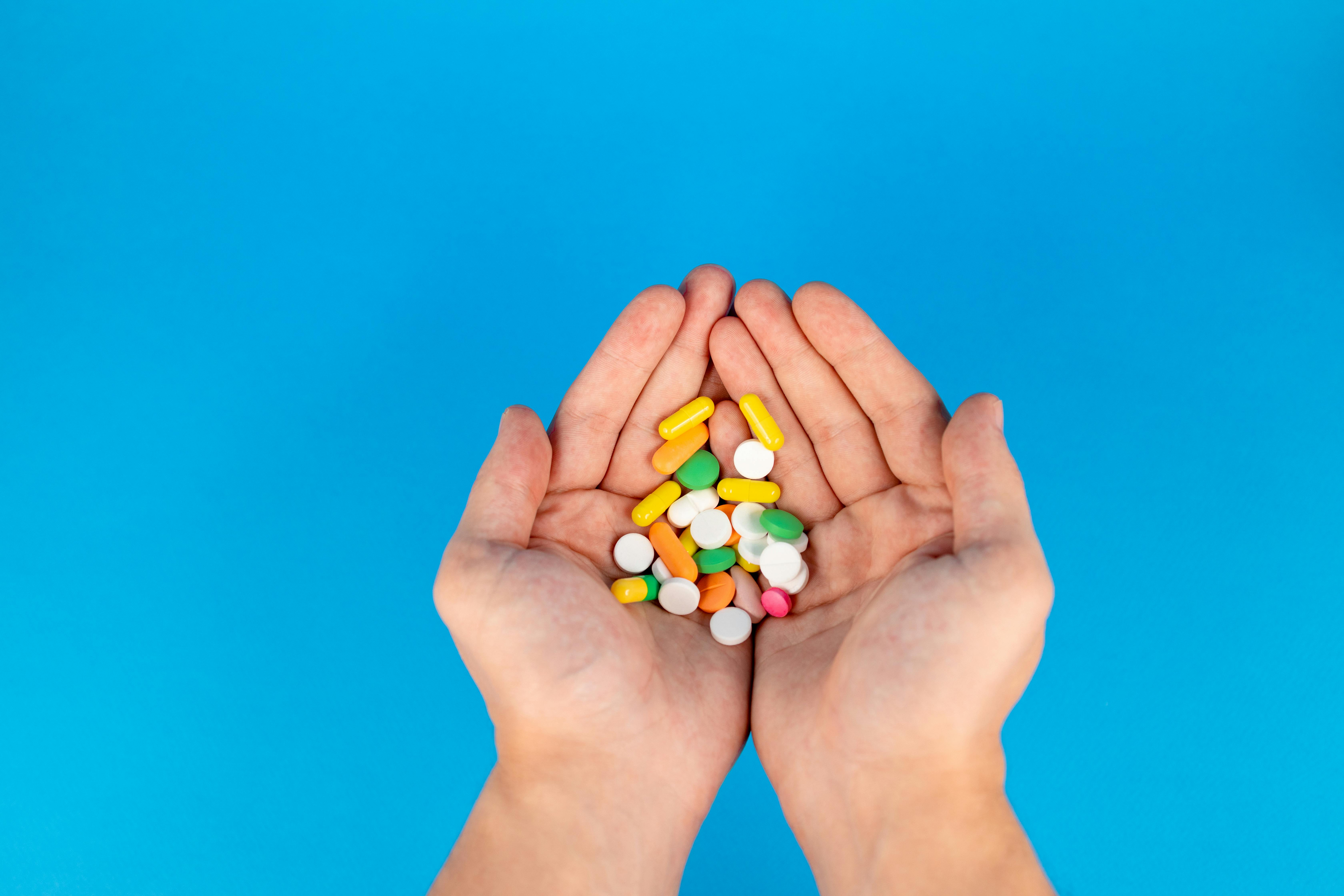 Hands holding a variety of colorful pills and tablets on a blue background, symbolizing medication and healthcare, relevant to the 340B Rebate Model Pilot discussion.